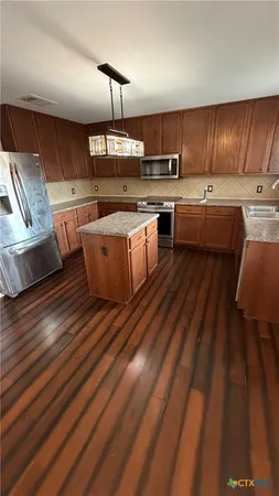 a kitchen with stainless steel appliances wooden floors wooden cabinets a sink and a stove
