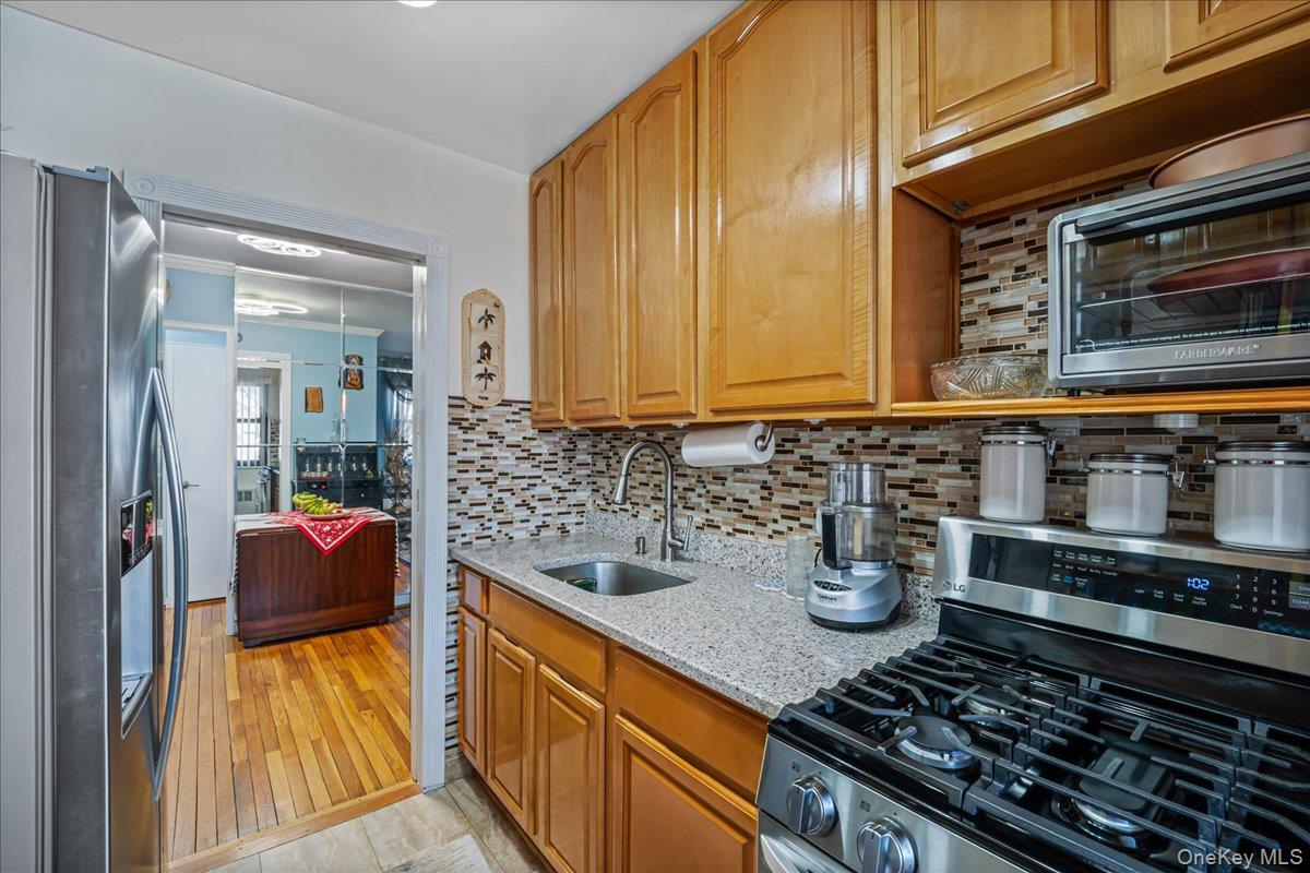 155-14 86th Street, Unit 2 Queens, NY 11414 - Photo 9 of 14 Kitchen with appliances with stainless steel finishes, light stone countertops, decorative backsplash, brown cabinets, and light wood-style flooring