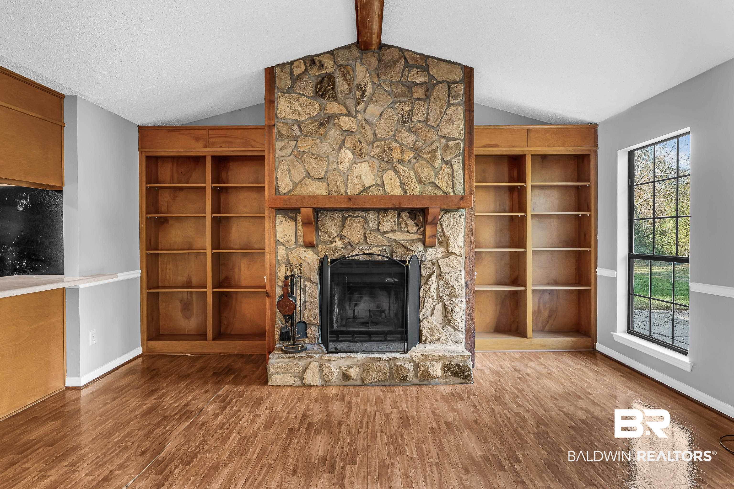 7787 Bellingrath Road Theodore, AL 36582 - Photo 13 of 36 Unfurnished living room featuring wood finished floors, a stone fireplace, and built in shelves