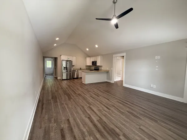 an empty room with wooden floor kitchen view and a window