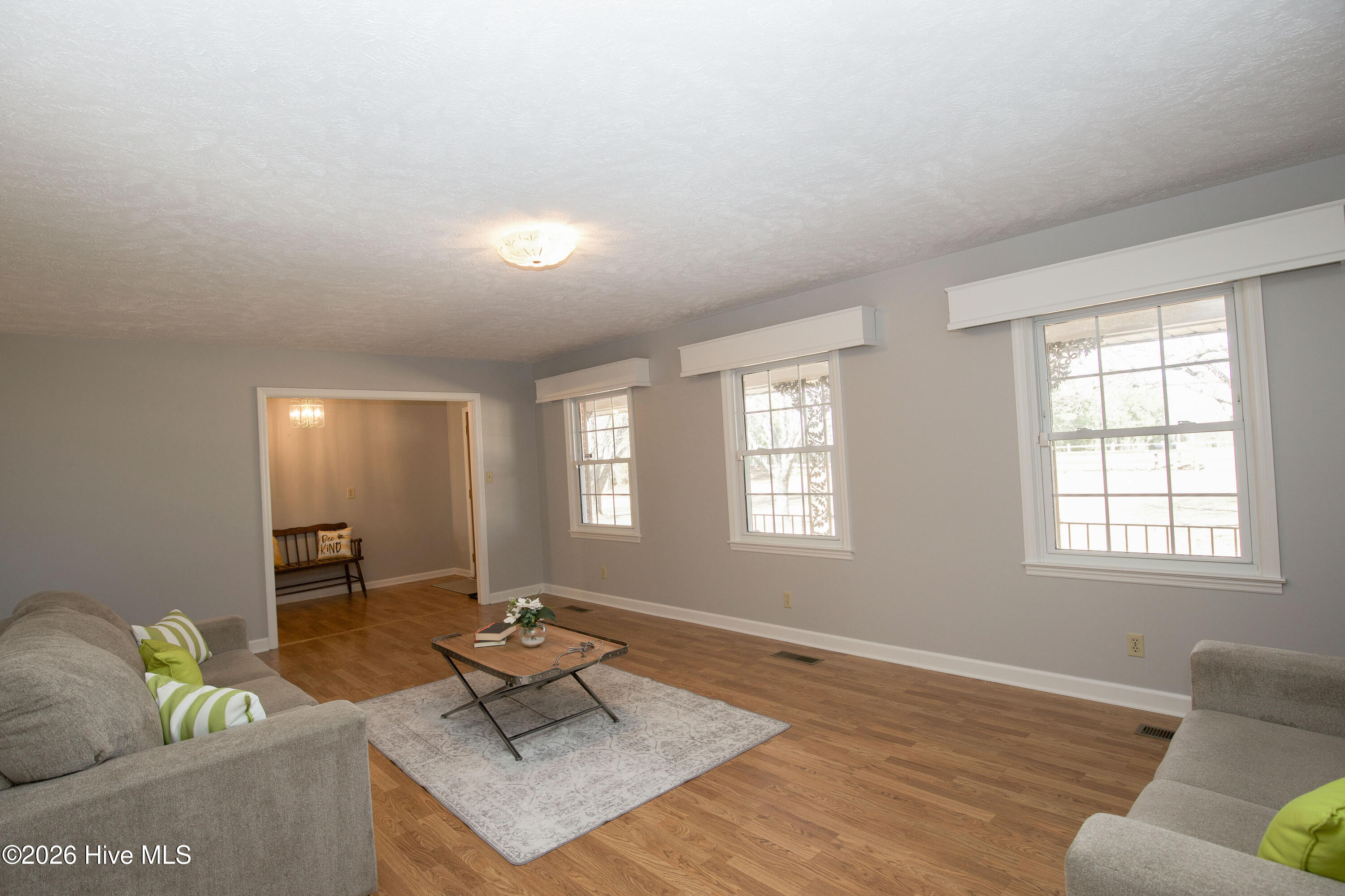 5068 Lobelia Road Vass, NC 28394 - Photo 10 of 70 This view showcases the smooth transition from the expansive living room to the welcoming foyer, enhancing the home’s inviting and functional layout. The flooring throughout offers the warm look of hardwood with easy upkeep, complementing the neutral color palette and abundant natural light. The classic wood front door and stylish light fixture add charm to the entry, creating a warm and polished first impression.