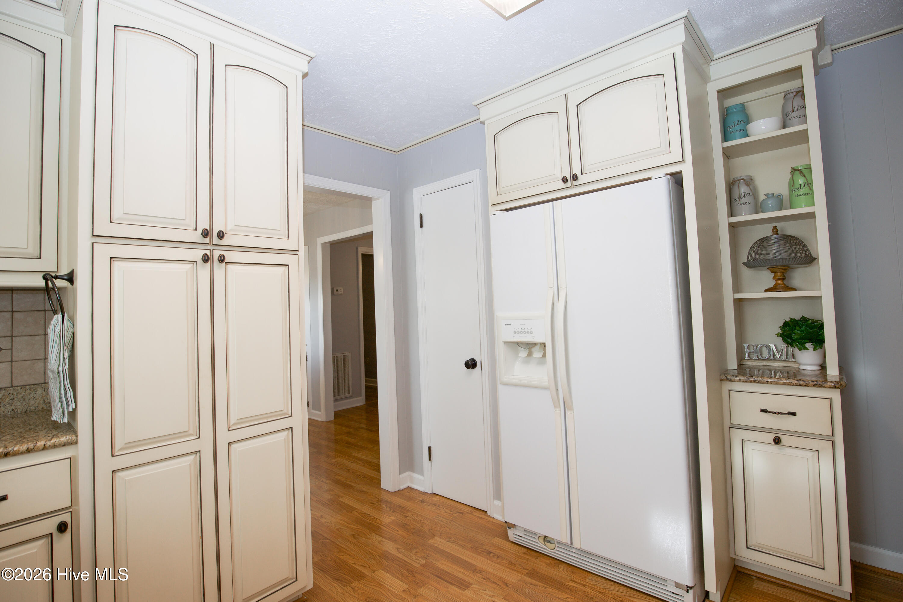 5068 Lobelia Road Vass, NC 28394 - Photo 14 of 70 This angle showcases the incredible storage options in the kitchen, including two oversized pantry cabinets and upper cabinetry extending to the ceiling. To the right of the refrigerator, a charming built-in shelving unit adds character and function—perfect for showcasing decor or storing essentials within easy reach. The white refrigerator complements the cabinetry seamlessly, and nearby access to the hallway enhances the flow of this efficient layout. From bulk grocery storage to your favorite kitchen accessories, there’s so much space to stay organized and stylish in this thoughtfully designed kitchen.