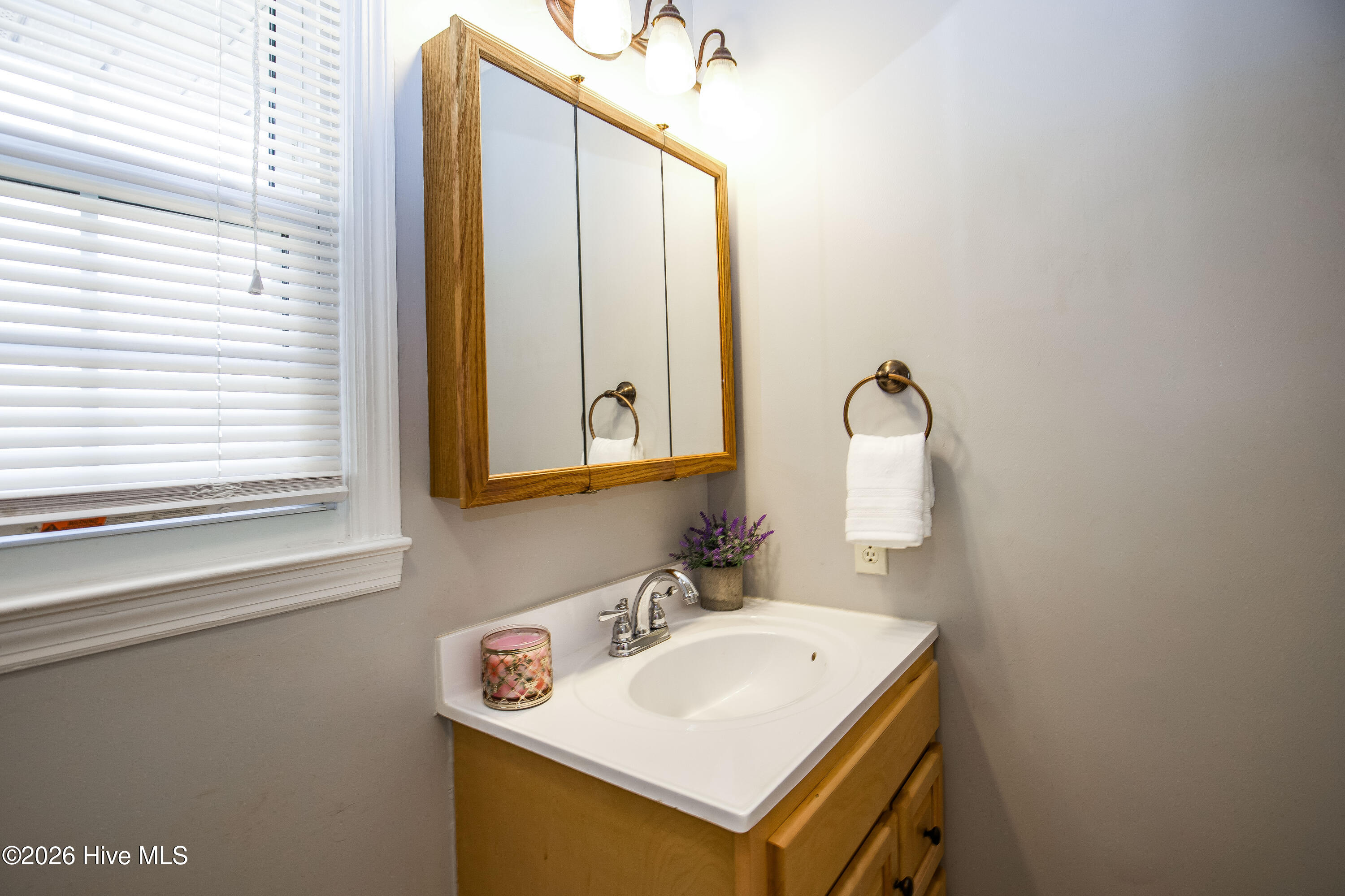 5068 Lobelia Road Vass, NC 28394 - Photo 22 of 70 The primary bathroom includes a bright vanity area with mirrored medicine cabinet, under-sink storage, and stylish bronze towel ring. Natural light from the window enhances the clean, functional space—ideal for everyday use.