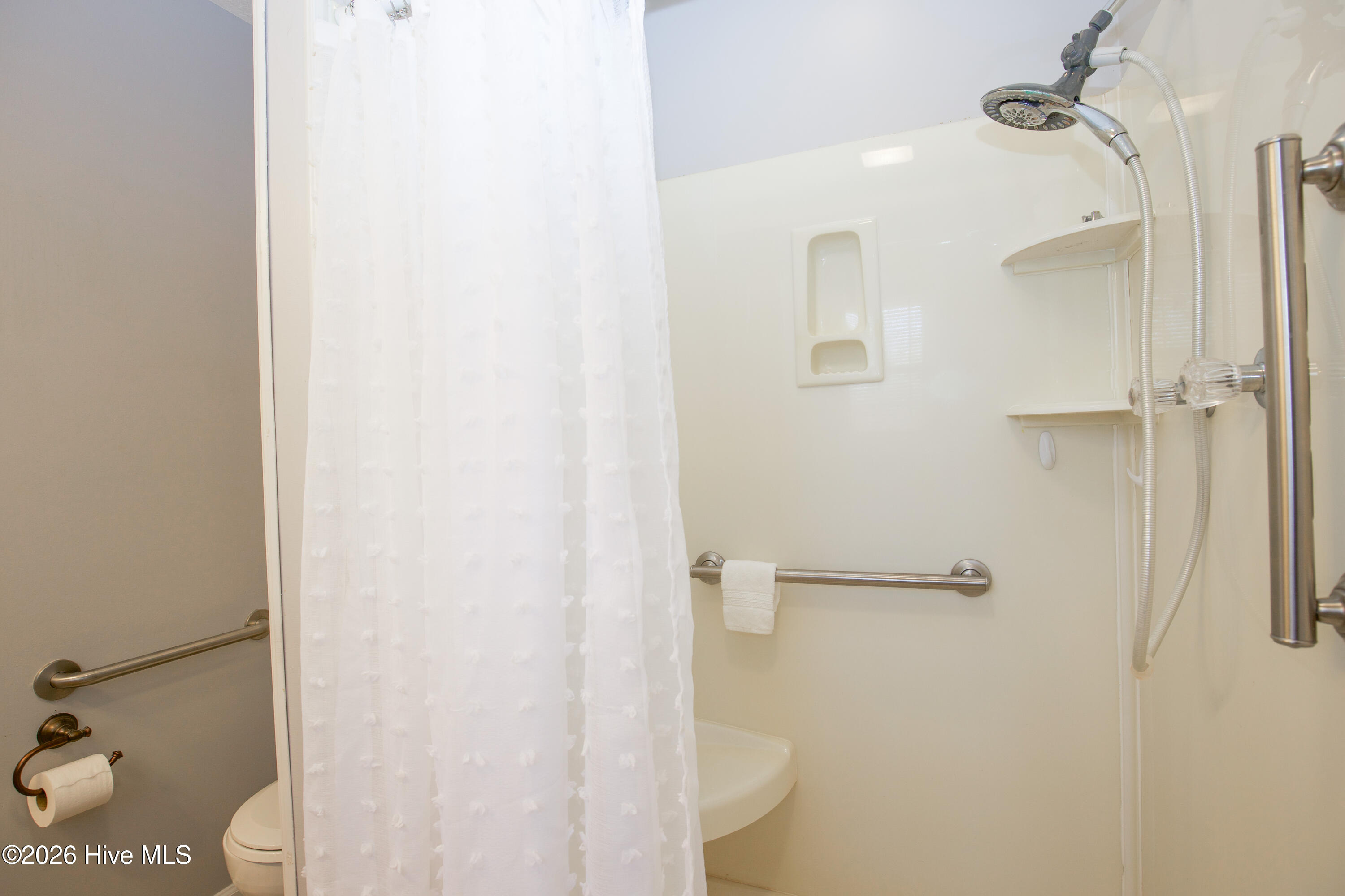 5068 Lobelia Road Vass, NC 28394 - Photo 24 of 70 Primary en-suite bathroom features a step-in shower with built-in seat and handheld showerhead, ideal for comfort and accessibility. Equipped with multiple grab bars for added safety and a neutral palette to match the rest of the home.