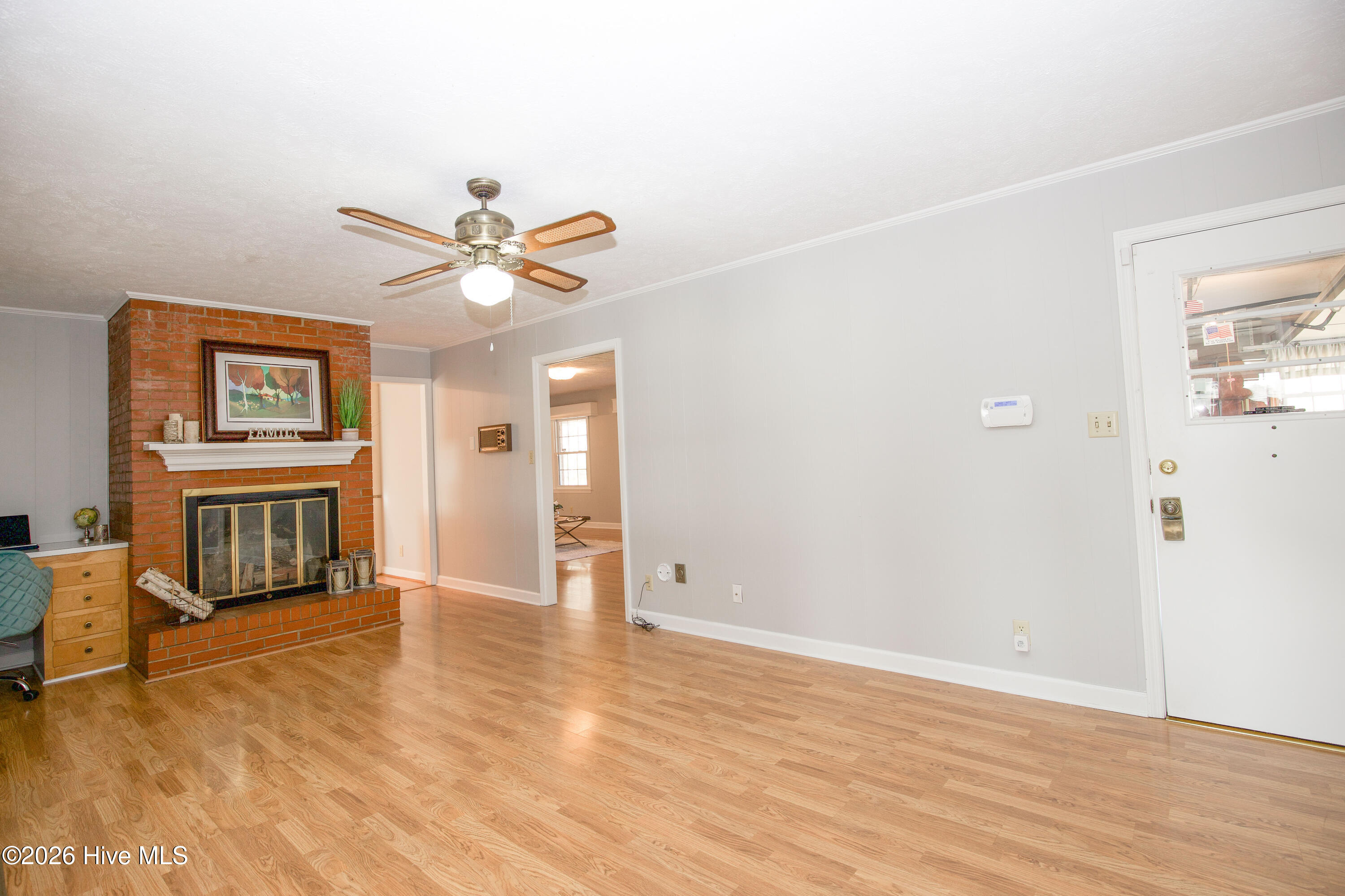 5068 Lobelia Road Vass, NC 28394 - Photo 27 of 70 Another view of the warm and inviting family room, featuring a classic brick fireplace with white mantle, built-in desk nook, and ceiling fan. The door to the right provides direct access to the garage, while the nearby hallway connects seamlessly to the living and Carolina rooms. This central space offers flexible functionality, perfect for gatherings, quiet evenings, or working from home.