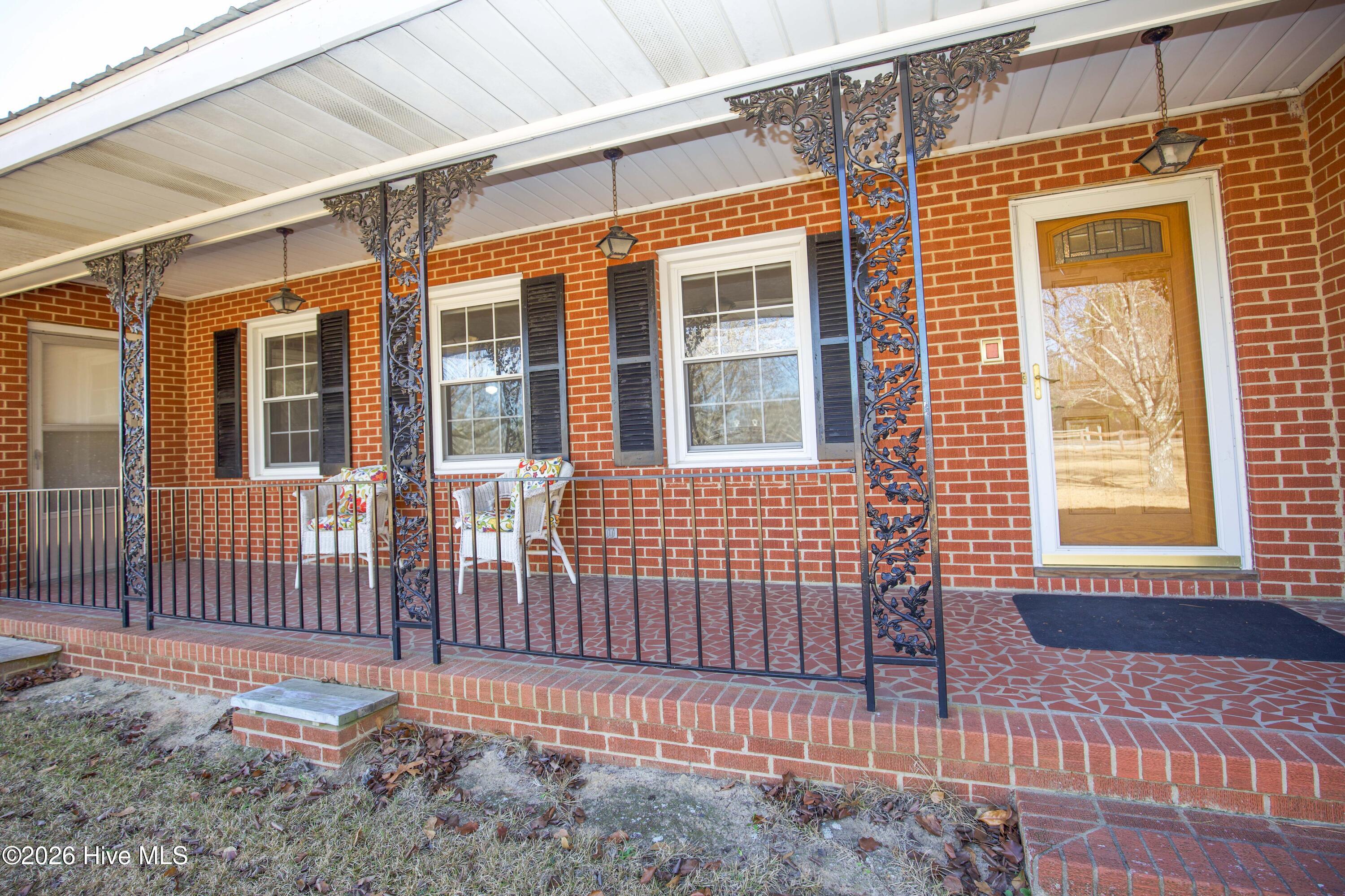 5068 Lobelia Road Vass, NC 28394 - Photo 2 of 70 Step onto the timeless brick front porch, highlighted by ornate wrought iron columns that add vintage character and curb appeal. The covered space offers a peaceful setting for morning coffee or evening relaxation with room for rocking chairs or a bistro set. Brickwork continues across the floor in a mosaic-style pattern, complementing the classic red brick exterior. This inviting entry sets the tone for the warmth and charm found throughout the rest of the home.