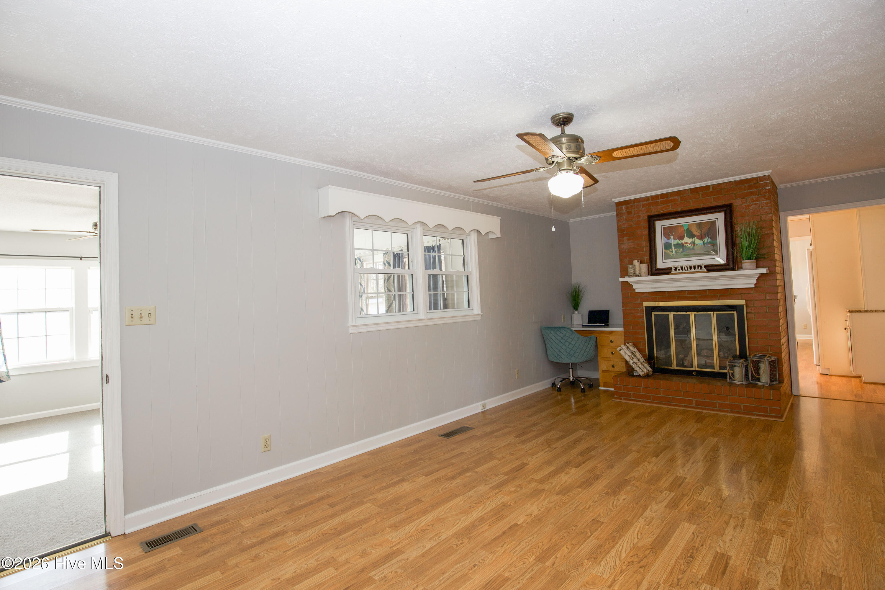 5068 Lobelia Road Vass, NC 28394 - Photo 30 of 70 Spacious family room featuring cozy brick fireplace and convenient built-in workspace. This central living area flows effortlessly into the Carolina Room on the left and the kitchen hallway on the right, offering exceptional connectivity throughout the home. Whether you're entertaining or enjoying a quiet evening, this is the heart of the home.
