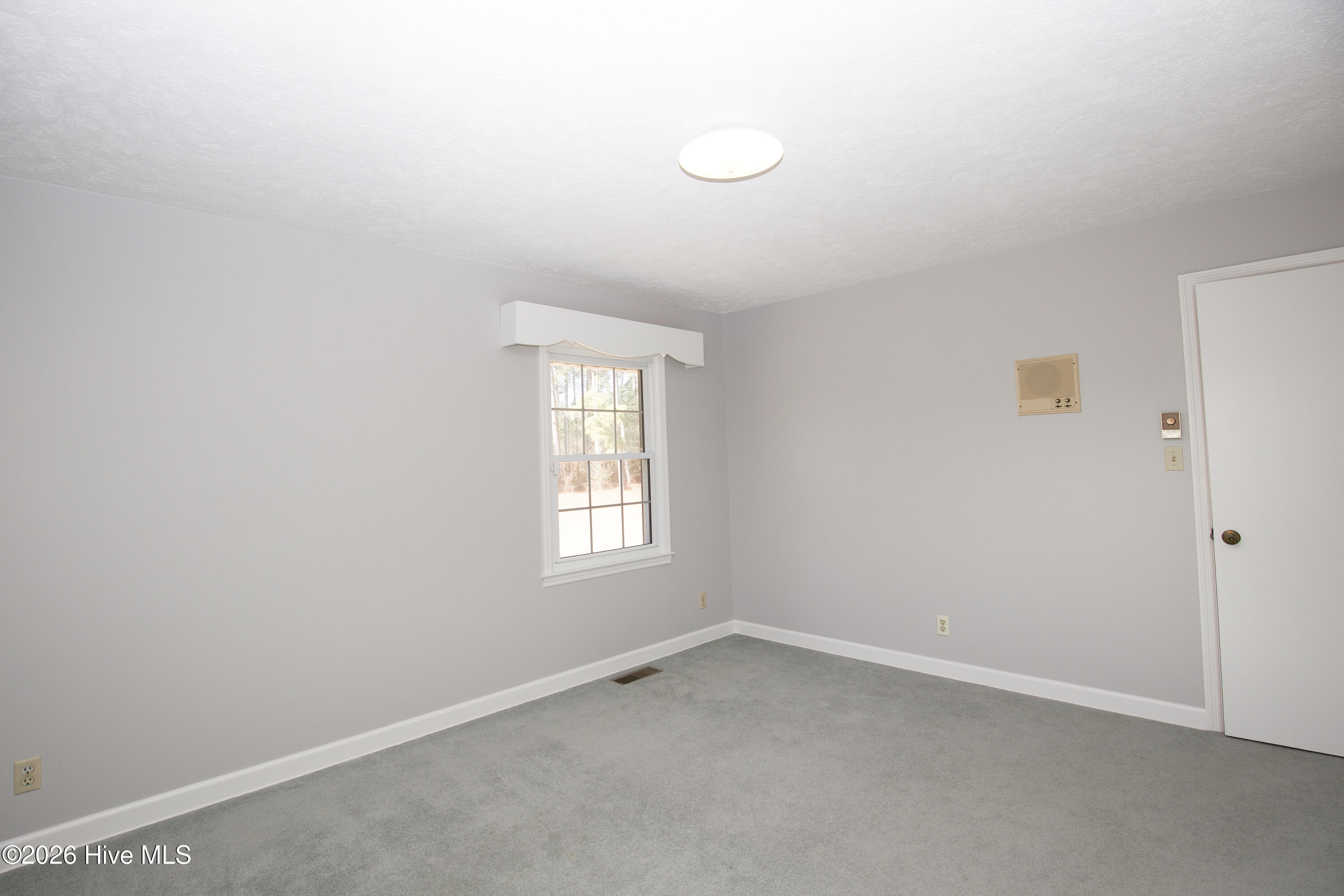 5068 Lobelia Road Vass, NC 28394 - Photo 38 of 70 Final angle of Bedroom #2, featuring soft carpeting, a large window with backyard views, and neutral tones for easy styling. A wall-mounted heater adds charm and comfort, while the room’s layout offers flexibility for use as a bedroom, office, or guest space.