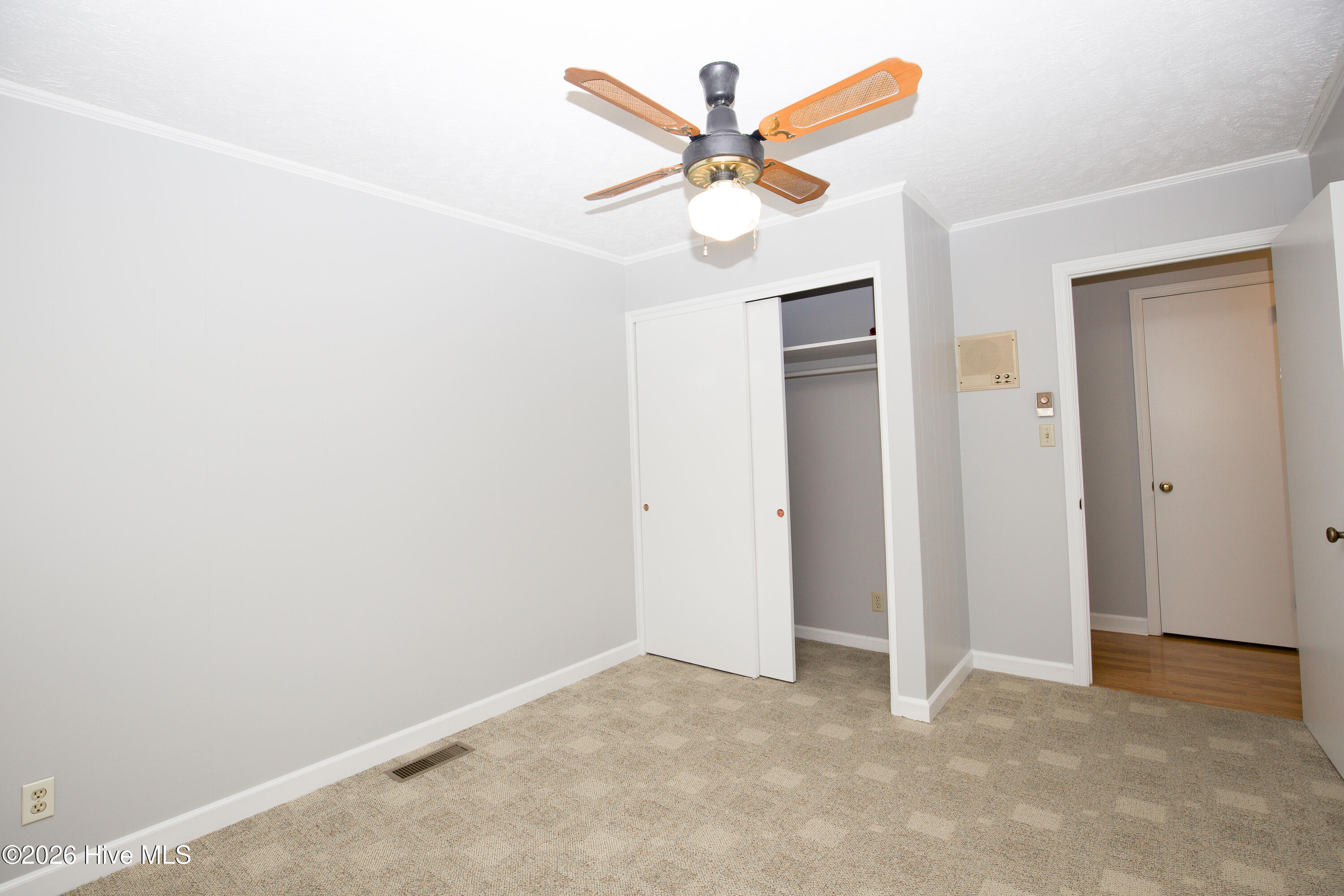 5068 Lobelia Road Vass, NC 28394 - Photo 39 of 70 Bedroom #3 with a view of the front yard, features a ceiling fan, plush neutral carpet, and a wide closet with sliding doors. A wall-mounted heater adds warmth, while convenient access to the hallway enhances its functionality as a bedroom, office, or guest space.
