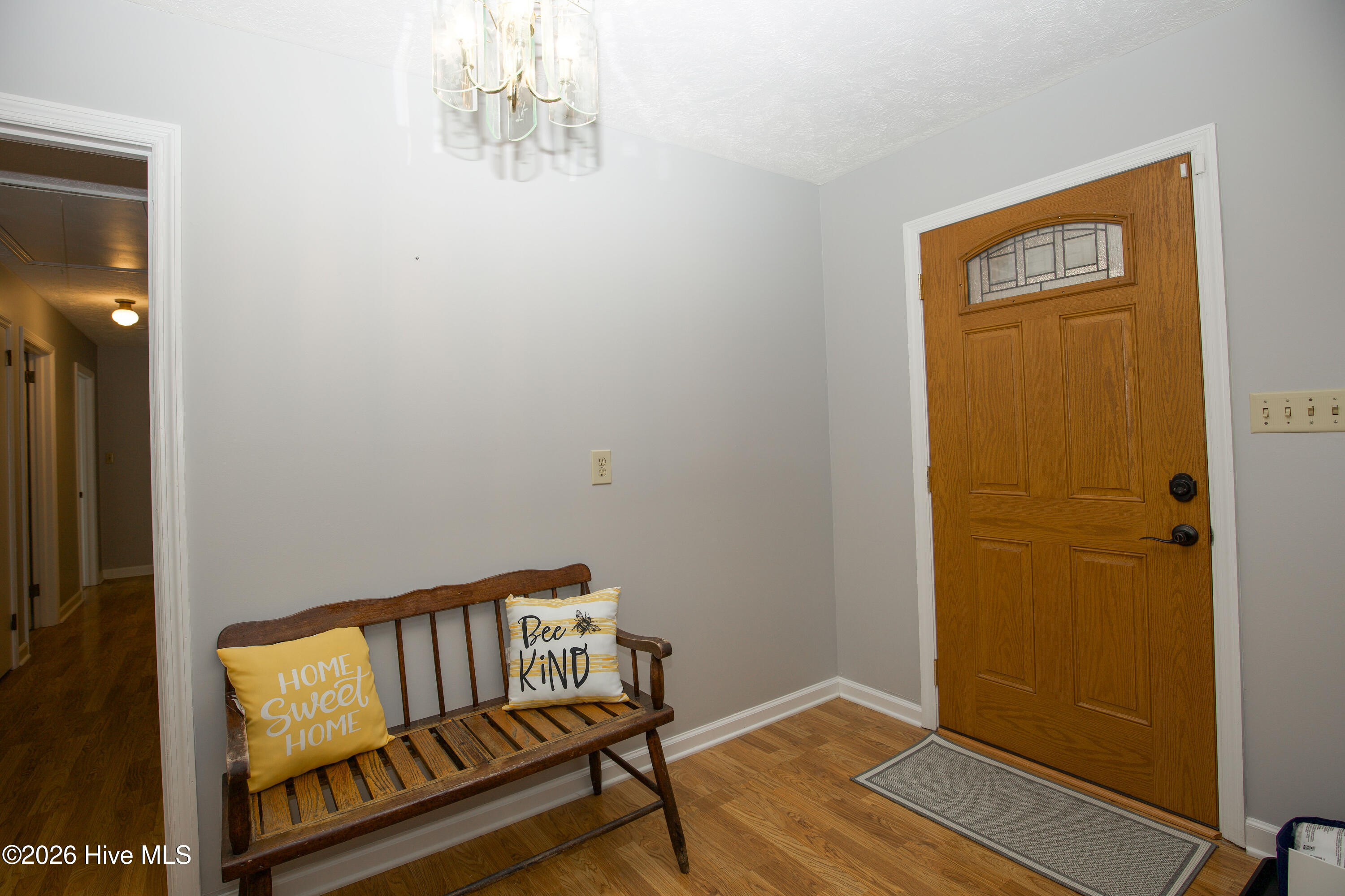 5068 Lobelia Road Vass, NC 28394 - Photo 4 of 70 Step inside to a bright and welcoming foyer that sets the tone for the rest of the home. The updated front door with decorative glass insert adds both charm and natural light. Neutral paint and durable flooring provide a clean, classic feel, while the overhead chandelier adds just the right touch of elegance. The bench seating area makes for a functional drop zone or a cozy place to greet guests. From here, you'll enjoy a smooth flow into the main living areas and hallway to the bedrooms—showcasing the thoughtful, traditional layout of this one-of-a-kind brick ranch.