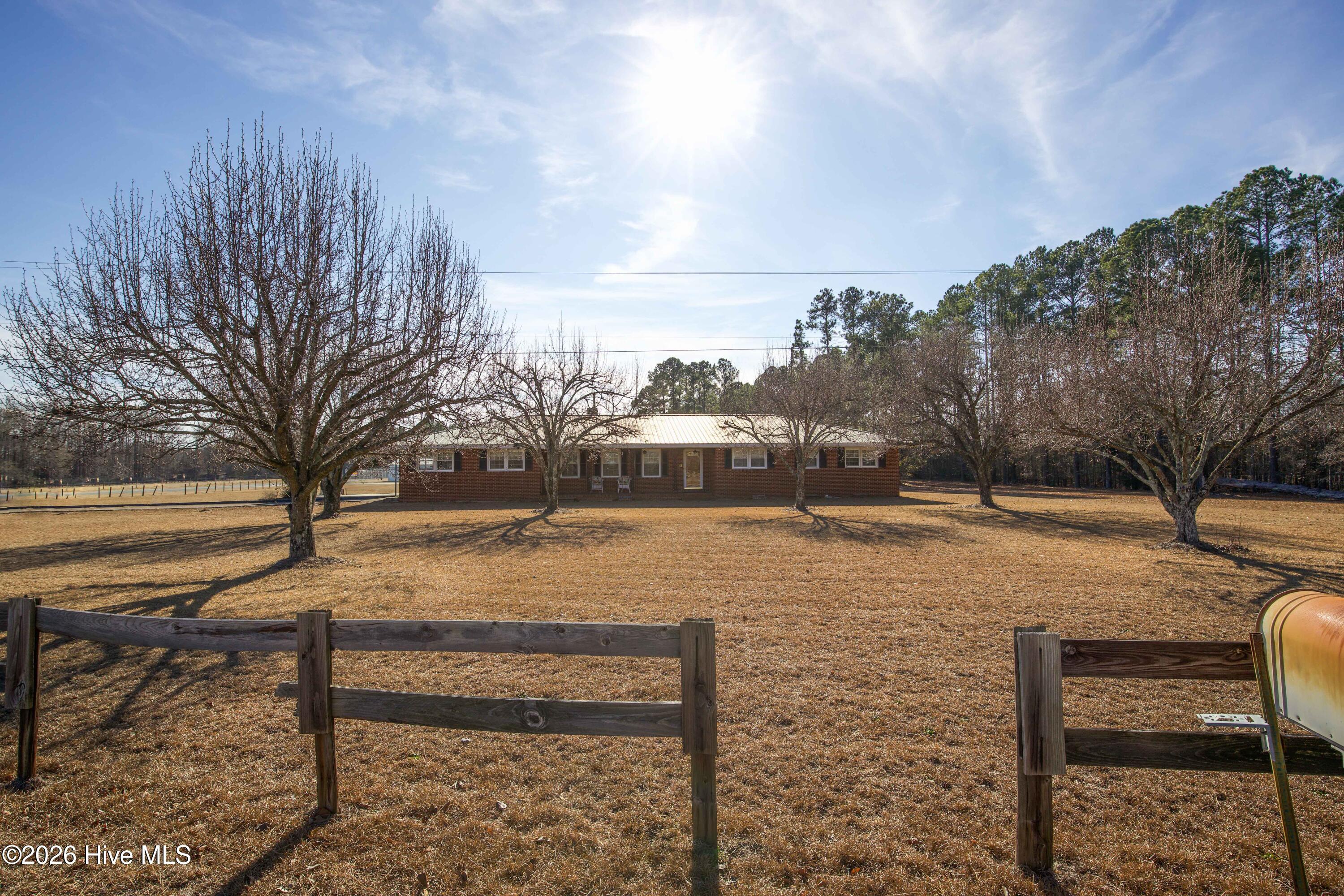 5068 Lobelia Road Vass, NC 28394 - Photo 55 of 70 This wide-angle view of 5068 Lobelia Rd highlights the generous front yard and peaceful rural setting in Moore County. Mature trees line the front of the property, offering natural shade and privacy. The home's long setback from the road provides added seclusion while maintaining a welcoming approach with a clear view of the classic brick façade. The setting delivers a balance of open space and established landscaping, perfect for enjoying nature or future landscaping ideas. Conveniently located near Fort Bragg, Southern Pines, and Sanford, the home combines country living with regional accessibility.
