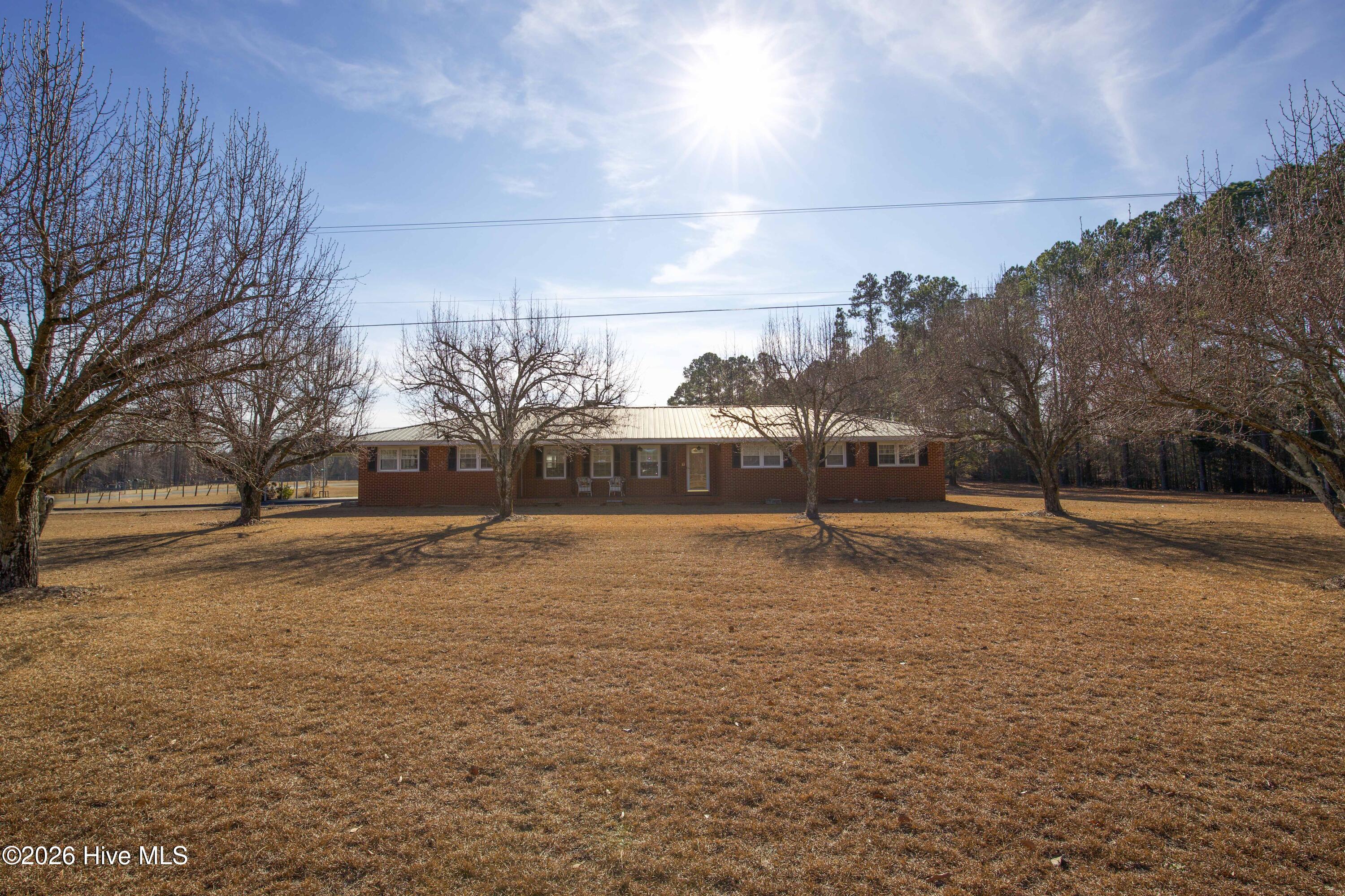 5068 Lobelia Road Vass, NC 28394 - Photo 56 of 70 A direct view of the full front elevation of 5068 Lobelia Rd, this image highlights the depth of the spacious yard, brick exterior, and symmetrical window design. The mature trees frame the home beautifully while maintaining clear sightlines to the covered front porch. Located in Moore County, the home offers peaceful country living with quick access to Fort Bragg, Southern Pines, and surrounding areas. The level lot and generous lawn create versatile outdoor possibilities for gatherings, gardening, or quiet enjoyment. This wide view reinforces the home's private yet accessible setting.