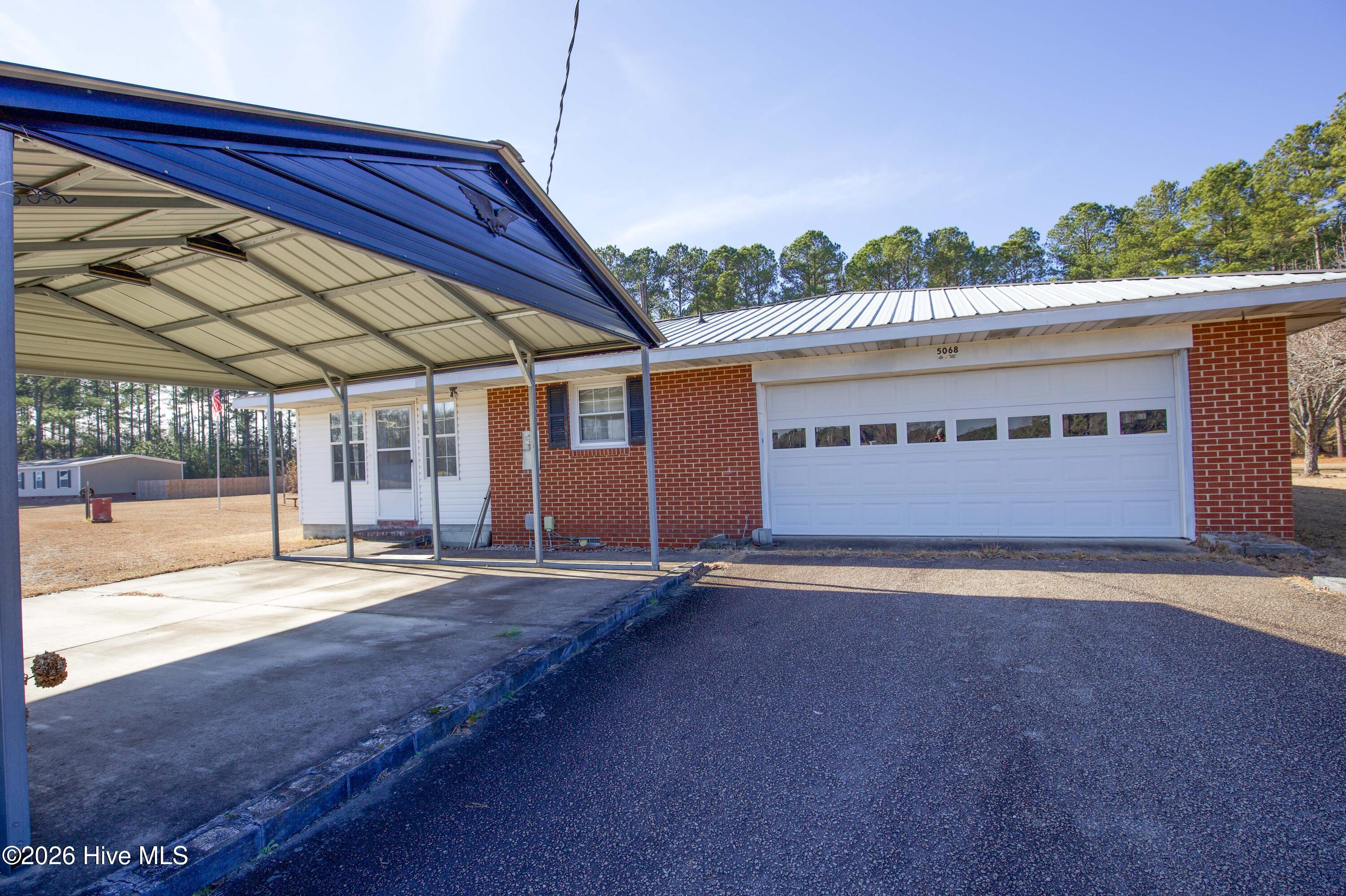 5068 Lobelia Road Vass, NC 28394 - Photo 61 of 70 This image highlights the paved driveway at 5068 Lobelia Rd, which leads to both a two-car attached garage and a metal-framed covered parking area. The front entry sits beneath a covered porch for weather-protected access into the home. Positioned on a corner lot with frontage along Wright Rd, this setup offers practical convenience for multiple vehicles or guests. The brick and siding exterior complements the metal roof, enhancing durability and curb appeal in rural Moore County.