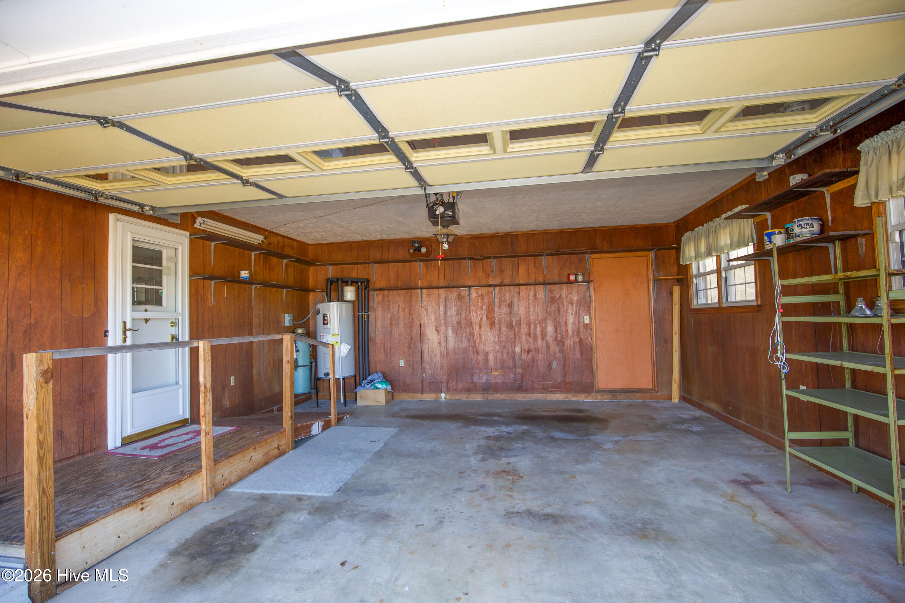 5068 Lobelia Road Vass, NC 28394 - Photo 62 of 70 Interior view of the spacious two-car attached garage at 5068 Lobelia Rd. This garage includes built-in shelving, pegboard walls for tool organization, and a ramped entry for easier accessibility to the main home. Natural light streams in through multiple windows, creating a bright and functional workspace or storage area. Also visible is the home's water heater, offering convenient utility access. Ideal for vehicle storage, hobby space, or workshop needs, this garage adds both practicality and flexibility to the property.