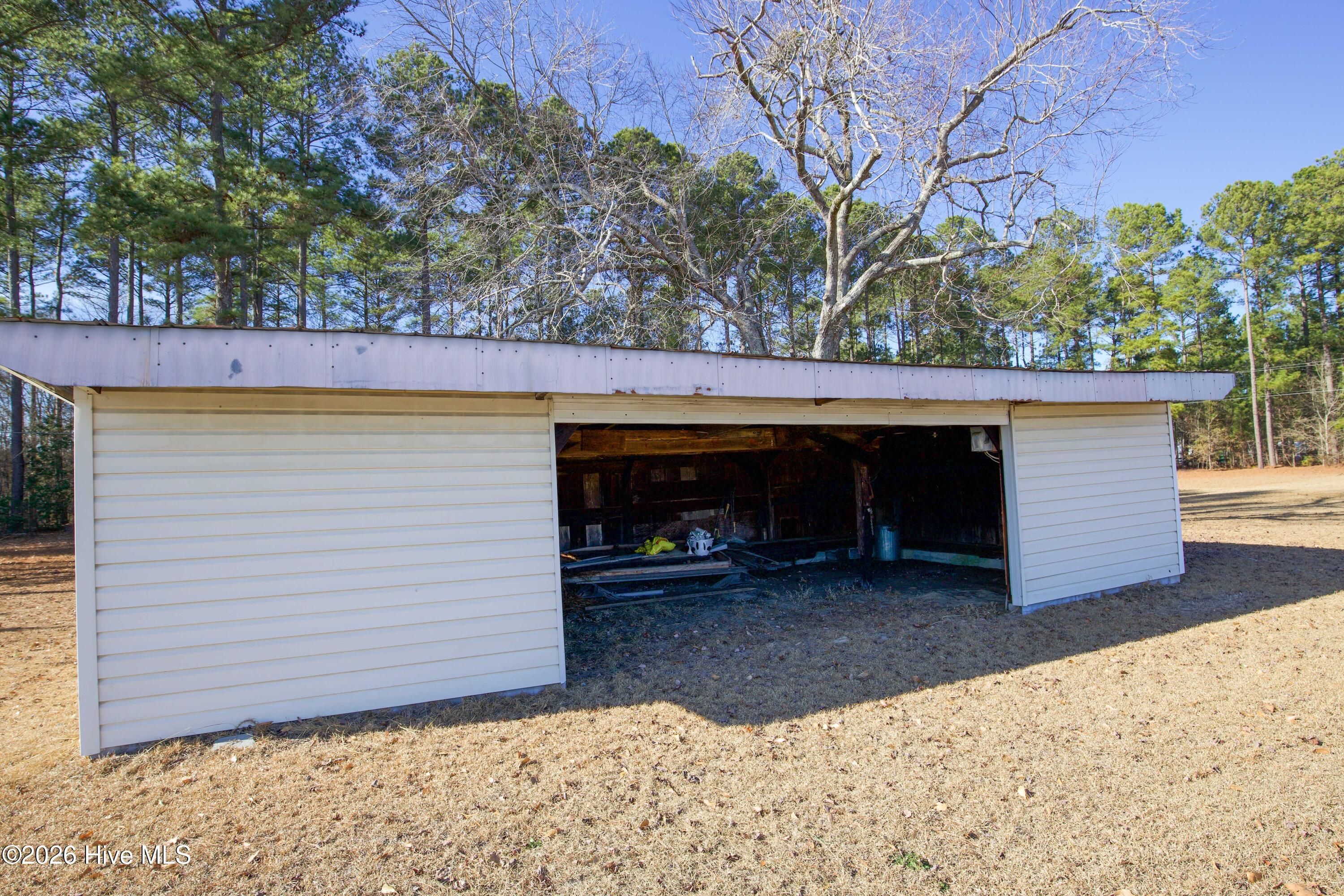 5068 Lobelia Road Vass, NC 28394 - Photo 65 of 70 This open-sided storage shed sits along the tree-lined rear of the property at 5068 Lobelia Rd. With partial enclosure and wood siding, it offers a practical space for housing yard tools or small equipment. Nestled beneath mature trees, the structure blends into the natural surroundings while providing functional utility space. Ideal for additional outdoor storage or project use away from the main home.