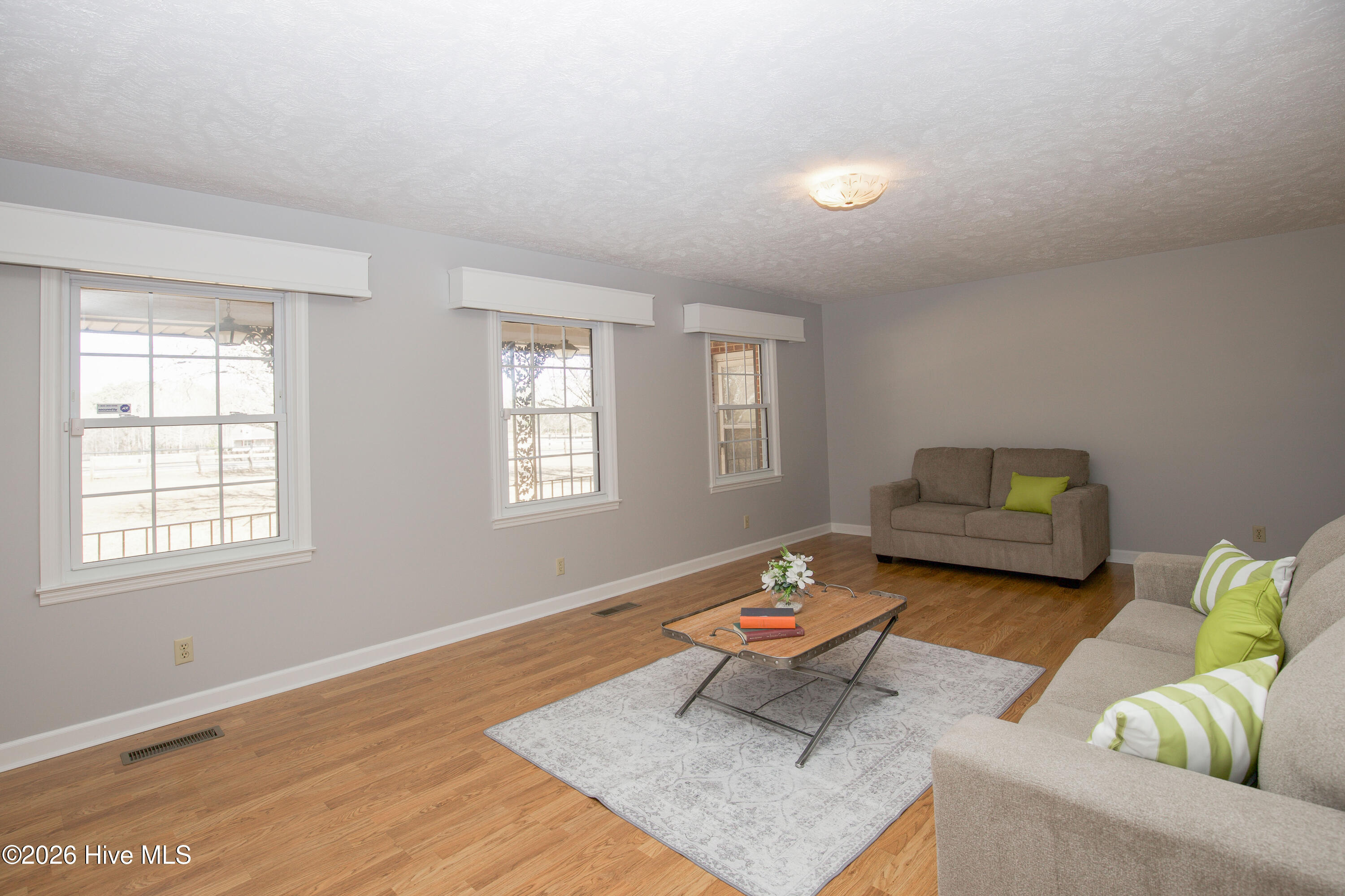 5068 Lobelia Road Vass, NC 28394 - Photo 8 of 70 Abundant natural light floods this spacious living room through three large, front-facing windows—offering scenic views and a bright, welcoming atmosphere throughout the day. Crisp neutral walls and rich-toned flooring create a modern yet warm canvas, ready to complement any design style. The layout easily accommodates both everyday living and entertaining, and the wide windows add charm while providing energy-efficient light and visibility. A perfect blend of comfort and functionality, this living space invites relaxation and conversation alike.