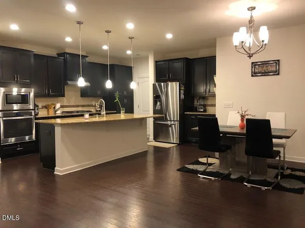 a kitchen with stainless steel appliances kitchen island granite countertop a refrigerator a stove a kitchen island a dining table and chairs with wooden floor