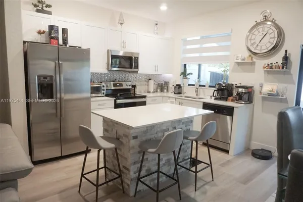 a kitchen with stainless steel appliances granite countertop a dining table chairs refrigerator and microwave