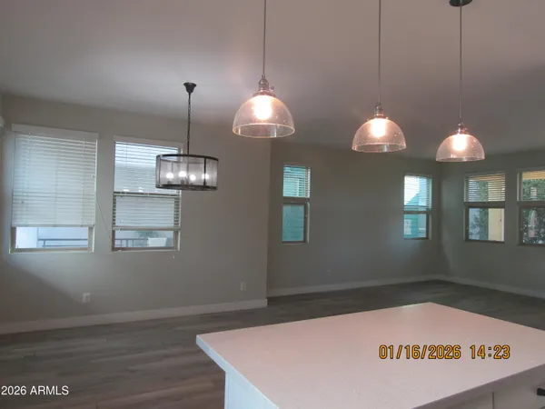 a view of an empty room with wooden floor chandeliers and kitchen view