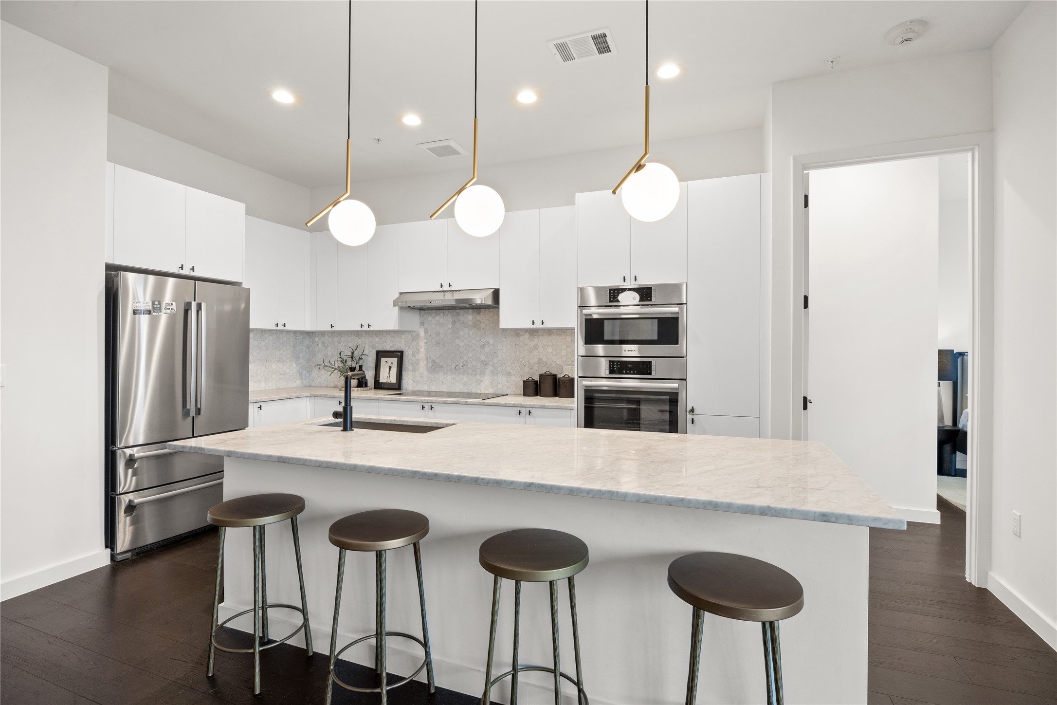 800 Embassy Drive, Unit 602 Austin, TX 78702 - Photo 10 of 37 Modern kitchen featuring an expansive island with stone countertop, stainless steel appliances, white cabinetry, and wood-finish flooring