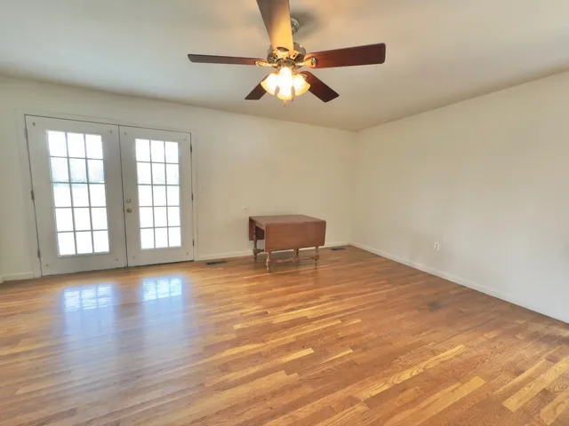 an empty room with wooden floor chandelier fan and windows