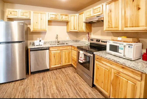 a kitchen with stainless steel appliances granite countertop a refrigerator a stove a sink and dishwasher with wooden floor