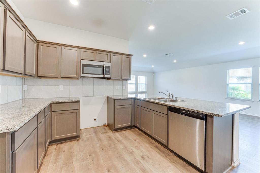 517 Milo Way Royse City, TX 75189 - Photo 2 of 34 Kitchen featuring wood-finish flooring, granite countertops, gray cabinetry, white subway tile backsplash, and stainless steel appliances including a microwave and dishwasher