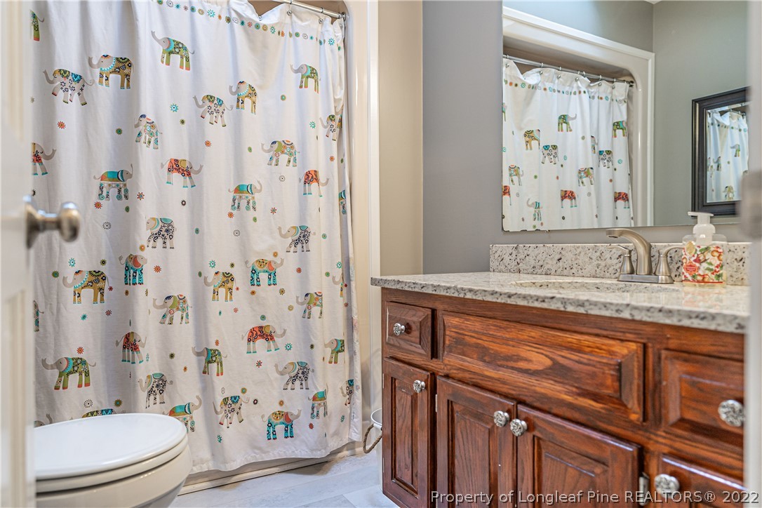 1075 Burning Tree Road Pinehurst, NC 28374 - Photo 16 of 25 a bathroom with a granite countertop sink a toilet and a shower curtain