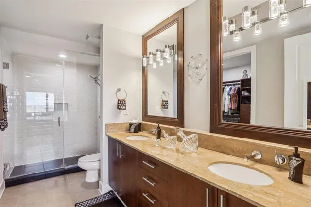 a bathroom with a granite countertop double vanity sink toilet mirror and shower