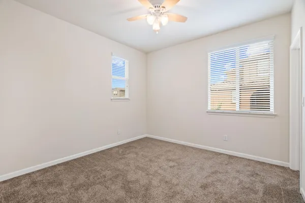 an empty room with chandelier fan and windows