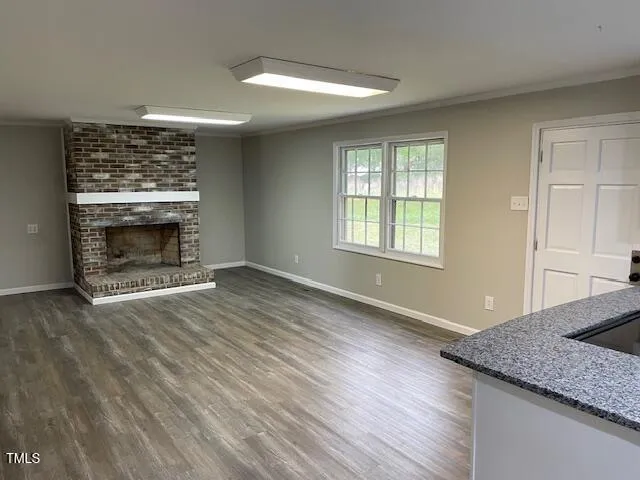 a view of an empty room with wooden floor fireplace and a window