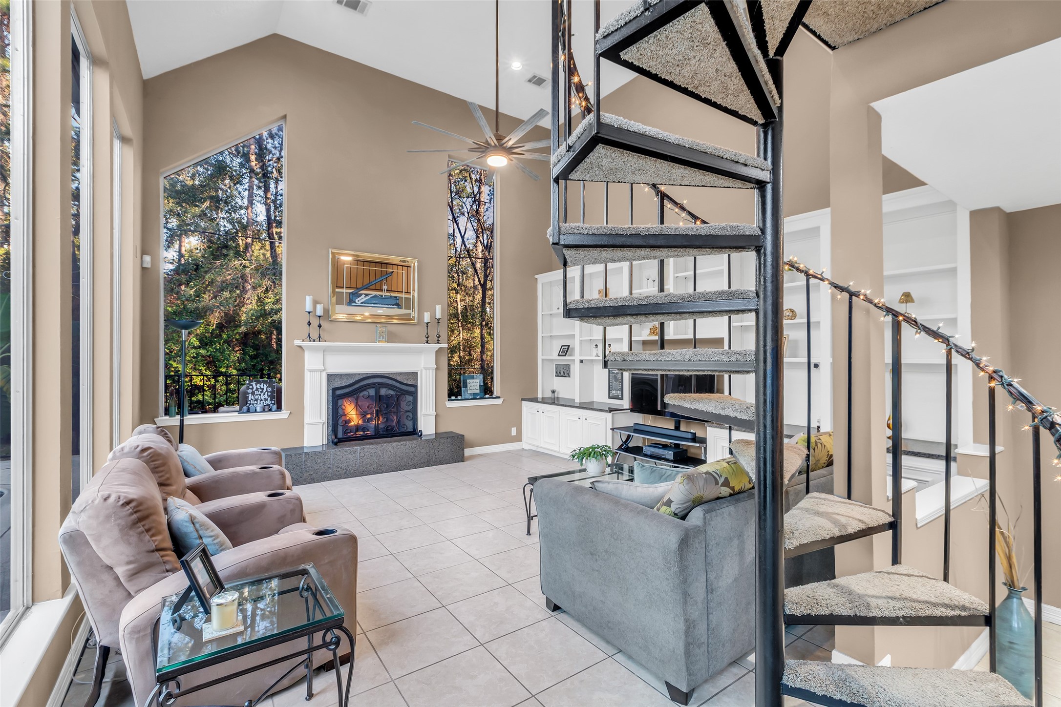 24102 Northcrest Drive Spring, TX 77389 - Photo 20 of 31 This inviting second family area features expansive windows, a cozy fireplace, and a stylish spiral staircase, offering a perfect blend of comfort and elegance for relaxed gatherings.