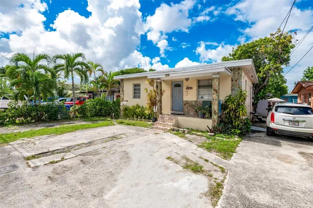 a view of a white house with a yard plants and a large tree
