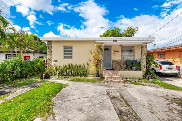 a view of a white house with potted plants and a large tree