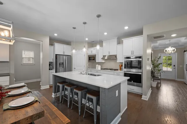 a kitchen with stainless steel appliances a stove a sink a refrigerator and white cabinets with wooden floor