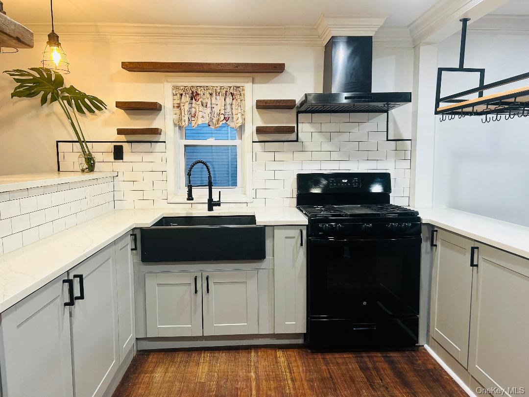 Kitchen with gas stove, ornamental molding, wall chimney range hood, backsplash, and open shelves