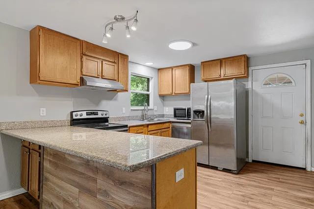 a kitchen with stainless steel appliances granite countertop a refrigerator a sink dishwasher a stove with wooden cabinets and floor