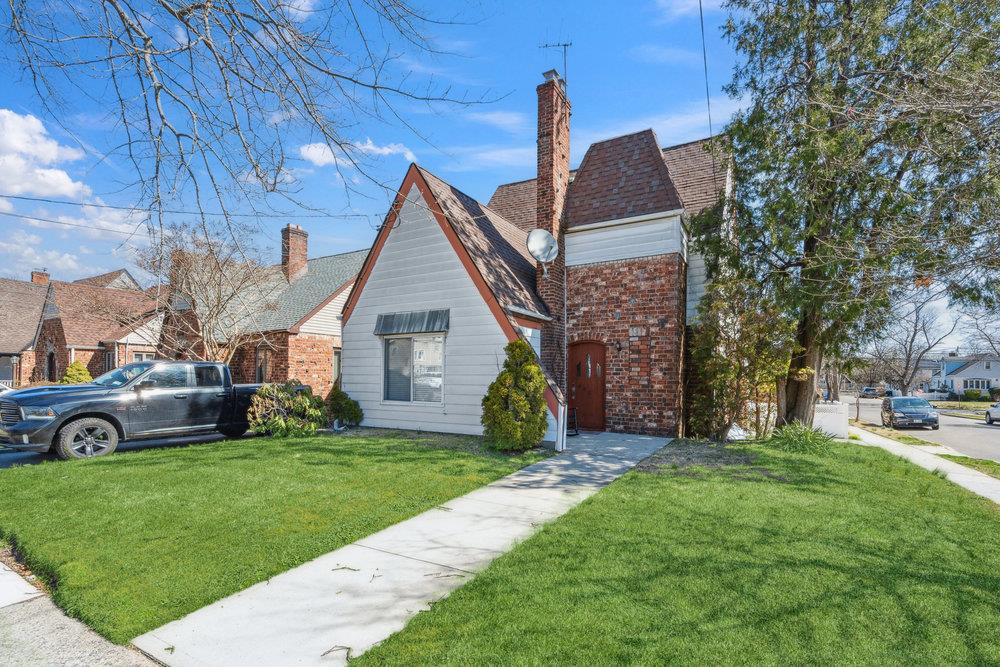 View of front of home featuring a chimney, brick siding, a shingled roof, and a front lawn