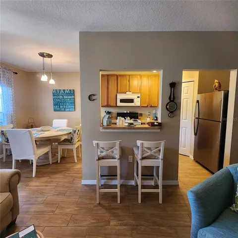 a kitchen with stainless steel appliances kitchen island granite countertop a dining table chairs and a refrigerator