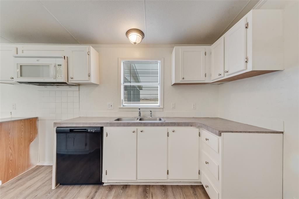 817 Kaufman Street Rosser, TX 75158 - Photo 13 of 29 Kitchen featuring black dishwasher, white cabinetry, light wood-type flooring, white microwave, and light countertops