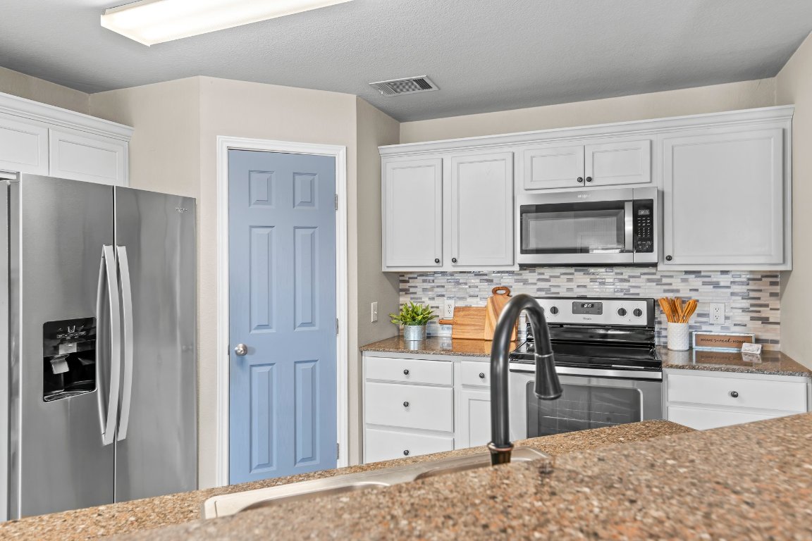 2201 Whistling Way Taylor, TX 76574 - Photo 26 of 40 Kitchen with appliances with stainless steel finishes, white cabinets and stone countertops