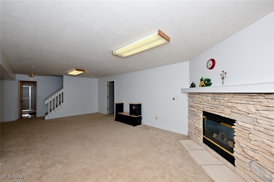 4212 Castle Ridge Akron, OH 44321 - Photo 36 of 44 Unfurnished living room featuring a stone fireplace, stairway, light carpet, and a textured ceiling
