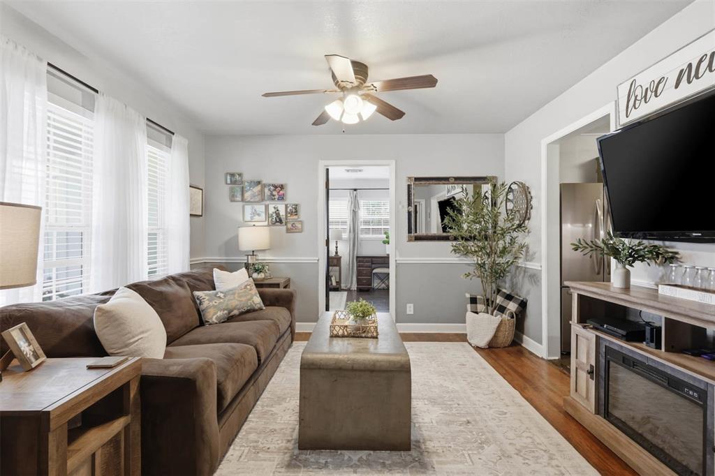 308 West 1st Street Springtown, TX 76082 - Photo 8 of 39 Living area featuring wood-finish flooring, two large windows with blinds, a ceiling fan with integrated lighting, and a two-tone wall treatment with wainscoting