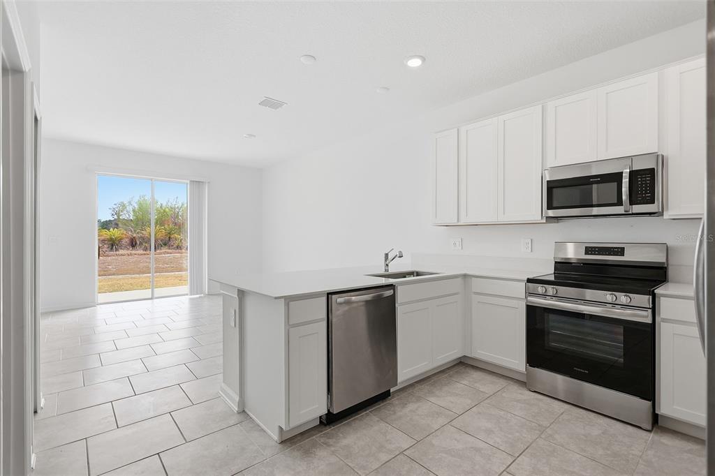 3303 Laurent Loop Davenport, FL 33837 - Photo 11 of 37 a kitchen with stainless steel appliances granite countertop a stove top oven a sink dishwasher and a refrigerator with wooden cabinets