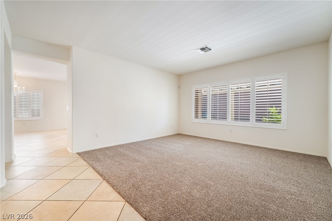 3033 Hartsville Road Henderson, NV 89052 - Photo 8 of 41 A versatile living area with neutral carpet and natural light from shuttered windows, seamlessly transitioning to tile flooring.
