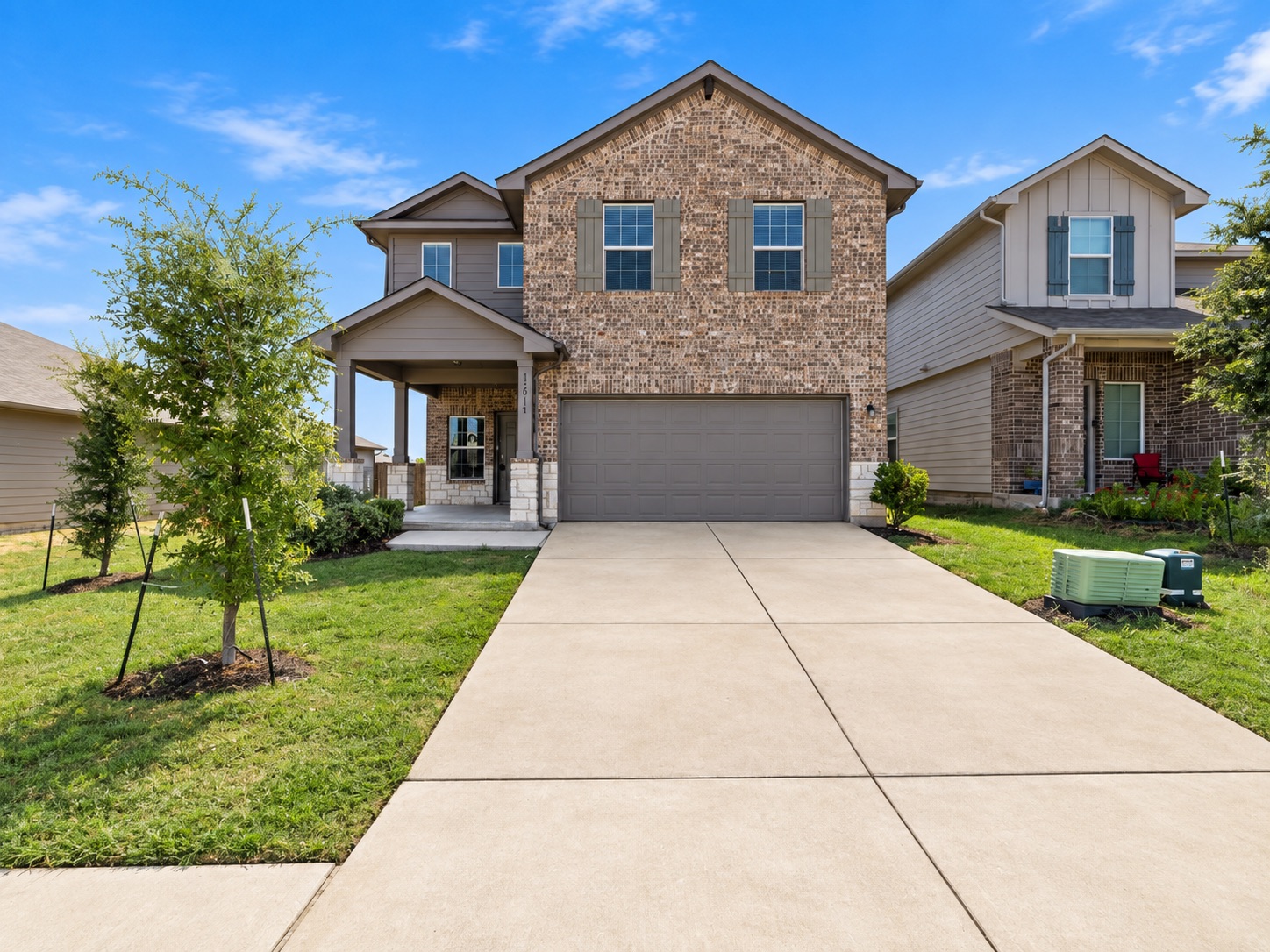 15011 Tuff Rd Manor Manor, TX 78653 - Photo 1 of 37 Two-story brick home with a covered front porch, attached two-car garage, and extended concrete driveway on a landscaped lot.