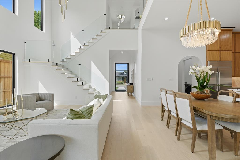 6038 Prospect Avenue Dallas, TX 75206 - Photo 14 of 40 Expansive open-concept living area featuring a dramatic floating staircase with glass railings, double-height ceilings, large windows, light wood-finish flooring, and a contemporary chandelier