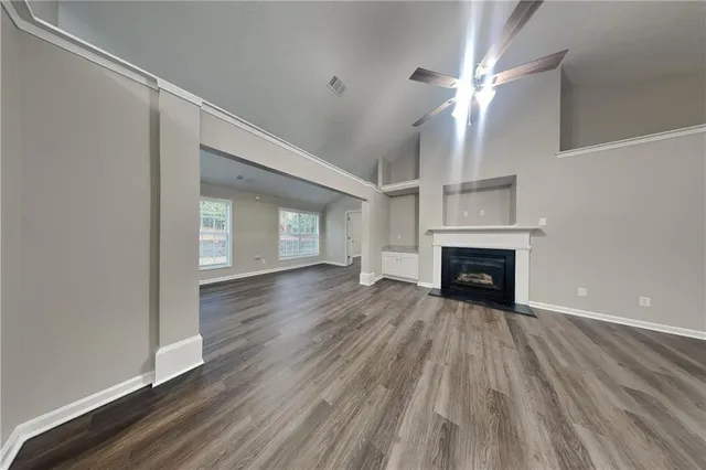 an empty room with wooden floor fireplace and windows