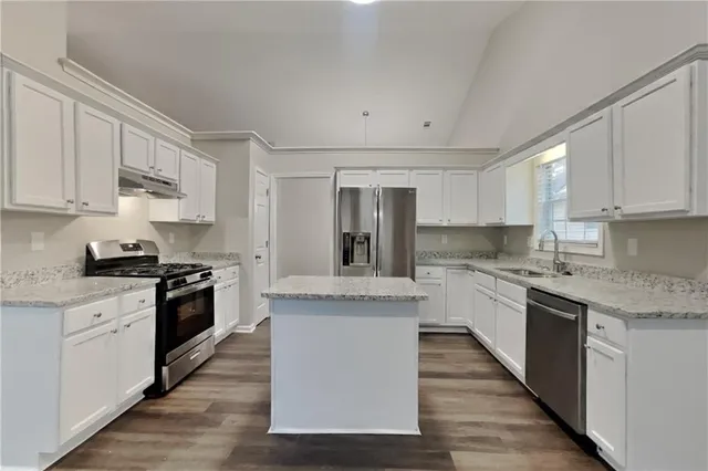 a large kitchen with granite countertop a stove top oven a sink dishwasher and white cabinets with wooden floor