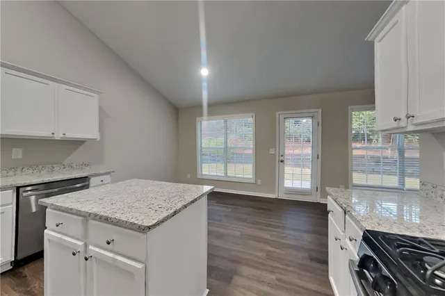 an empty room with wooden floor and kitchen view